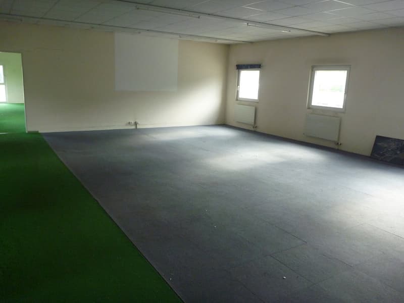 Empty room with green carpet, concrete flooring, windows, heaters, and a whiteboard mounted on the wall.