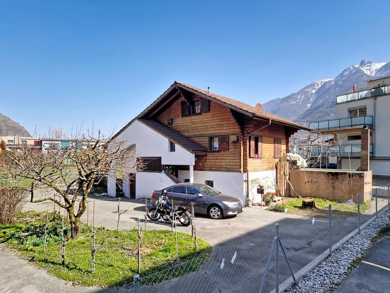 Detached house, wooden exterior, white walls, brown roof, garage, car and motorcycle parked in front, small garden, mountain view