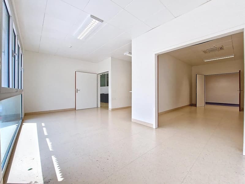 Empty room with white walls, tiled floor, large windows, and ceiling lights