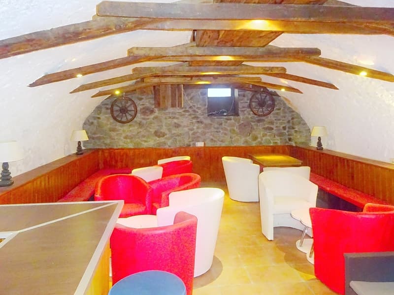 A room with wooden beams, stone walls, red and white chairs, wooden benches, lamps, a table, and a television.