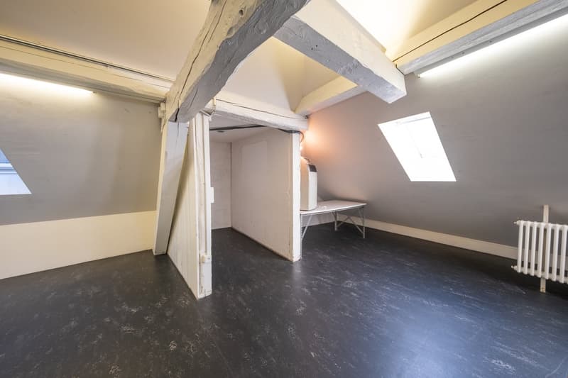 Wooden beams, white walls, black floor, open door, white radiator, table
