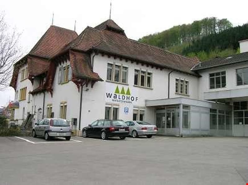 large white building, brown roof, several windows, cars parked in front