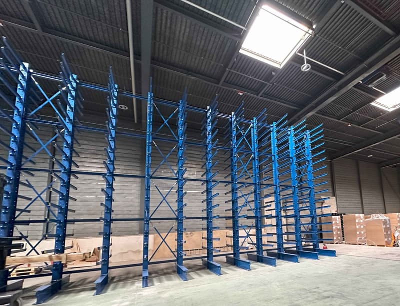 Large industrial warehouse with rows of blue metal shelving units for storage and organization of goods and materials.