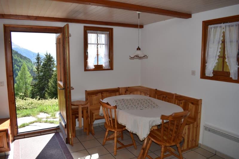 Wooden dining table with chairs, wooden bench seating, wooden ceiling beams, large windows with a view of the mountains and forest outside