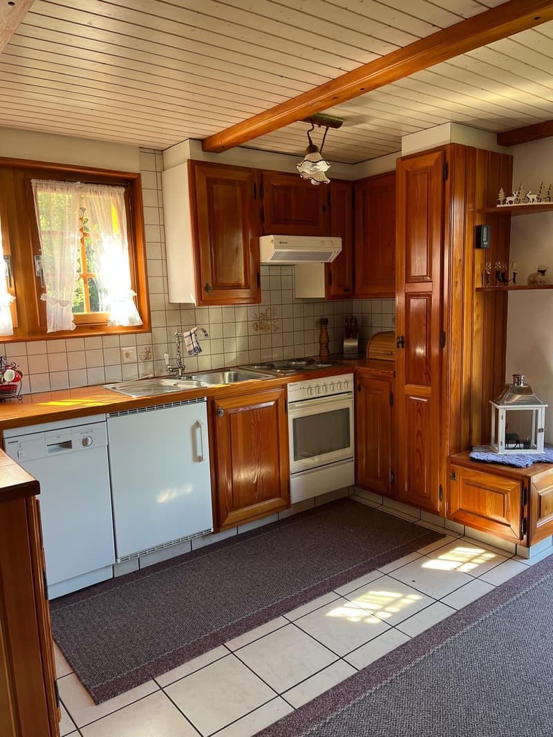 Wooden cabinets, tile backsplash, gas stove, dishwasher, sink, window, wooden ceiling beams