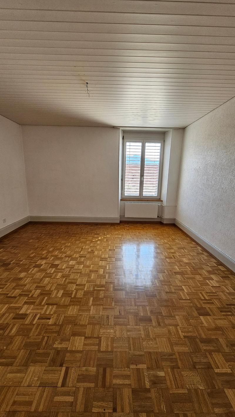 Empty room, wooden parquet flooring, white walls, white ceiling, a window with blinds, and a white radiator