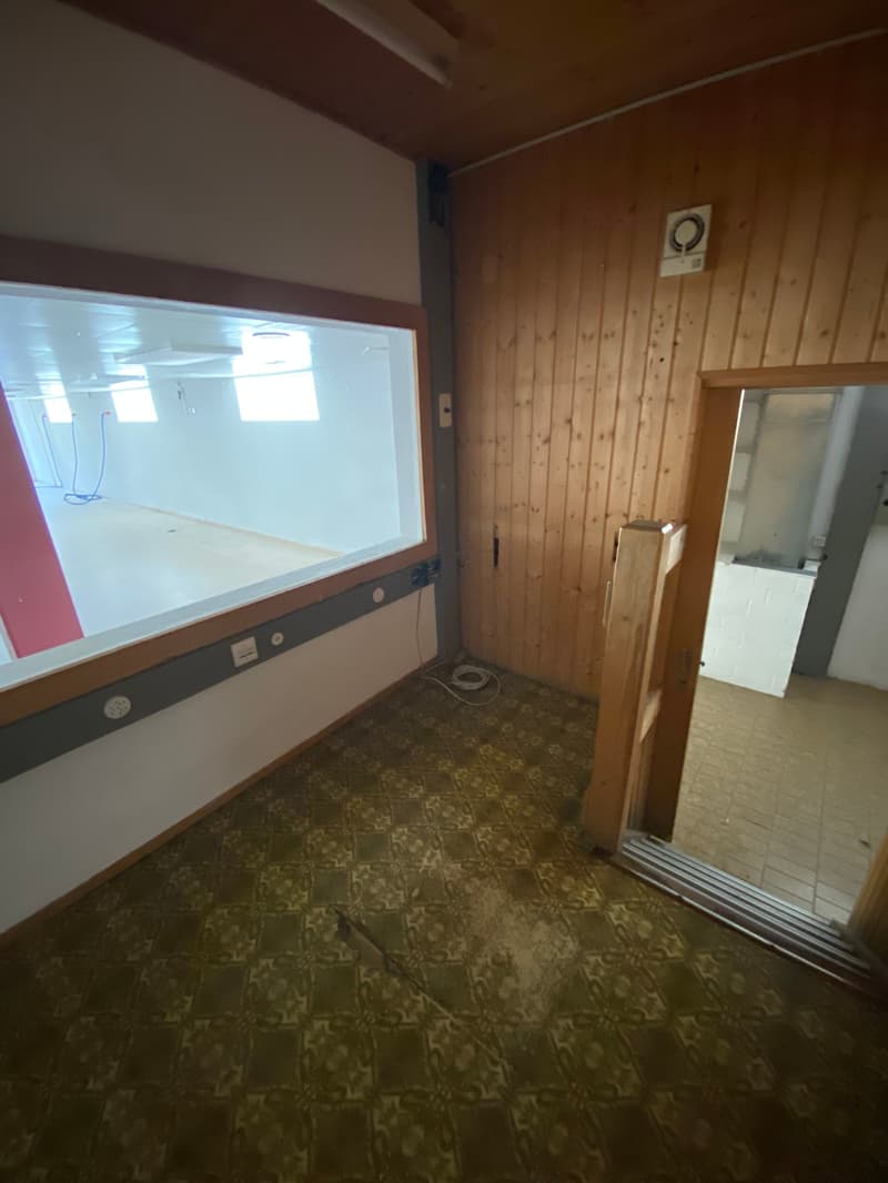 The image shows a small room with wooden paneled walls, a tiled floor, and a washing machine visible through a glass window. The room appears to be a laundry or utility space.