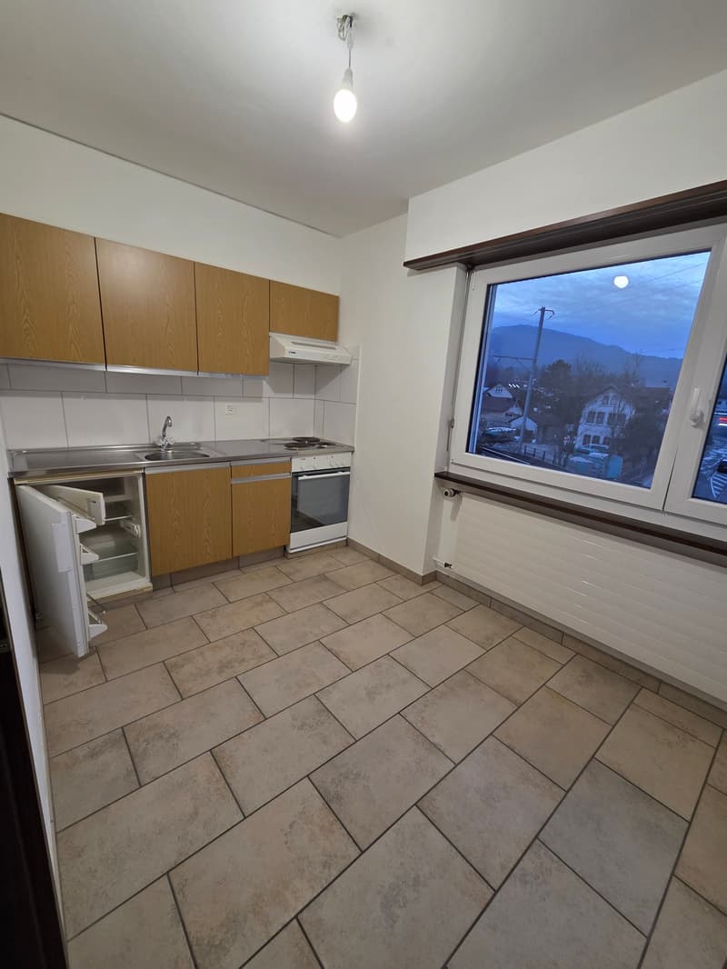 Empty kitchen with a sink, stove, and refrigerator. Large window.