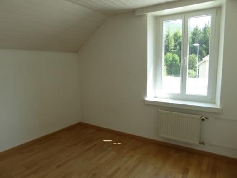 Spacious bedroom with hardwood flooring, white walls, and a large window providing natural light.