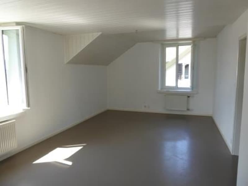 Spacious bedroom with white walls, hardwood flooring, and large windows allowing natural light to enter the room.