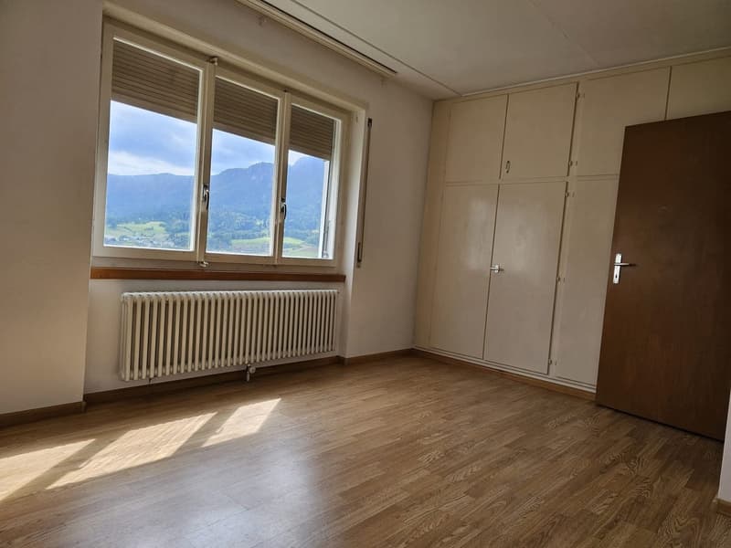 empty room with a large window with blinds, wooden floor, large radiator, wooden door, wardrobes