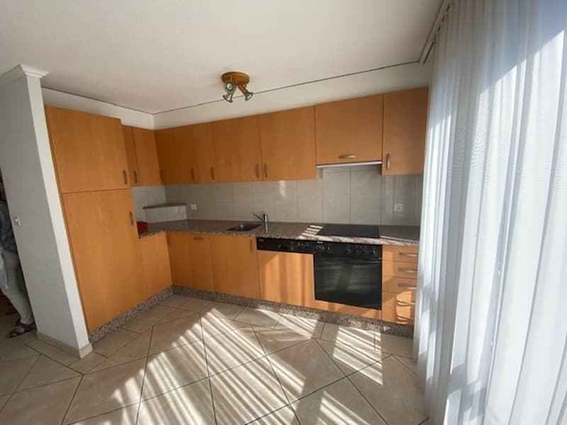 Open-plan kitchen with wooden cabinets, tiled floor, white curtains, black oven, stove, sink