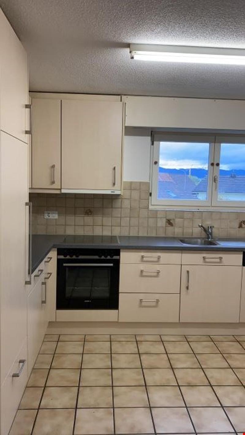 Modern kitchen with white cabinets, tiled floor, black countertops, electric oven, sink, window