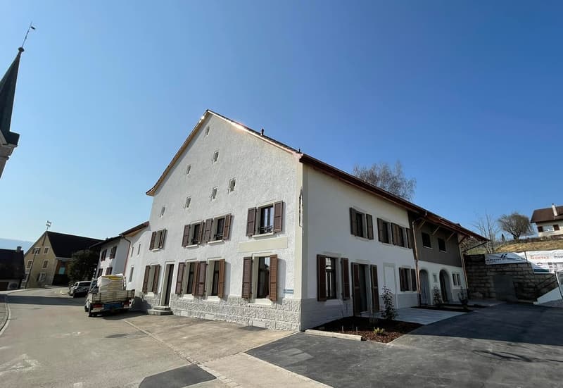 white multi-story building with brown shutters, paved parking area