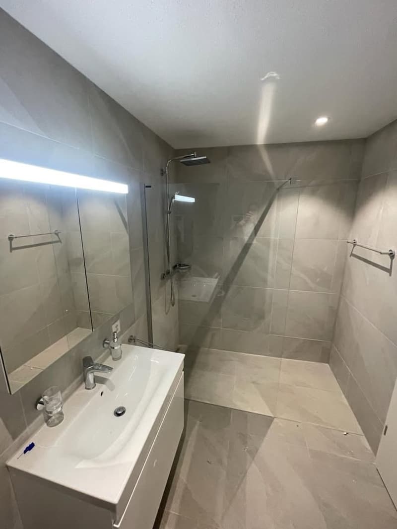 modern shower stall, white sink, tiled flooring, mirror, wall-mounted faucet, power outlet