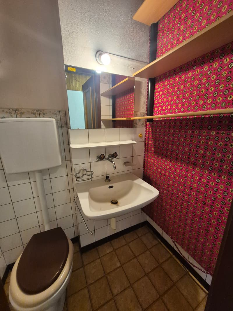 bathroom: sink, toilet, mirror, tiled floor, tile walls, light