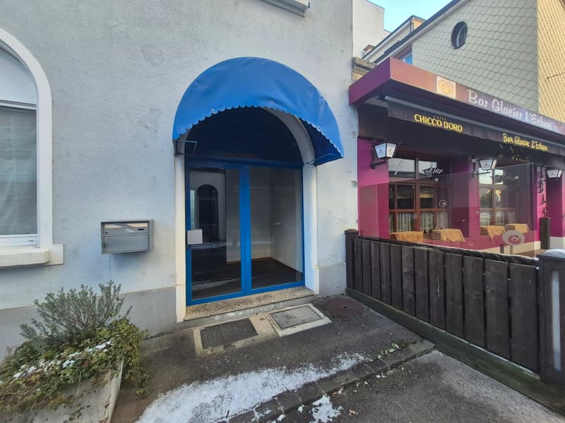 white building, blue awning, mailbox, closed entrance door, black fence, window with white trim, snow on the ground