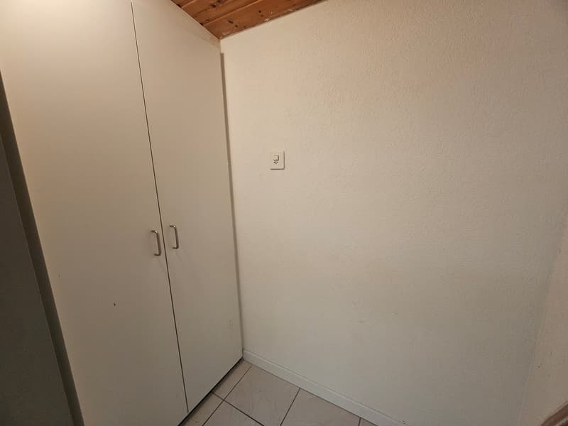 A small room with a closet and white tiles