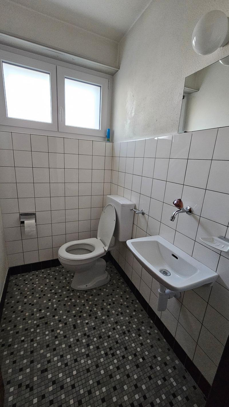 Bathroom with toilet, sink, wall-mounted faucet, and mirrors, and tiled floor