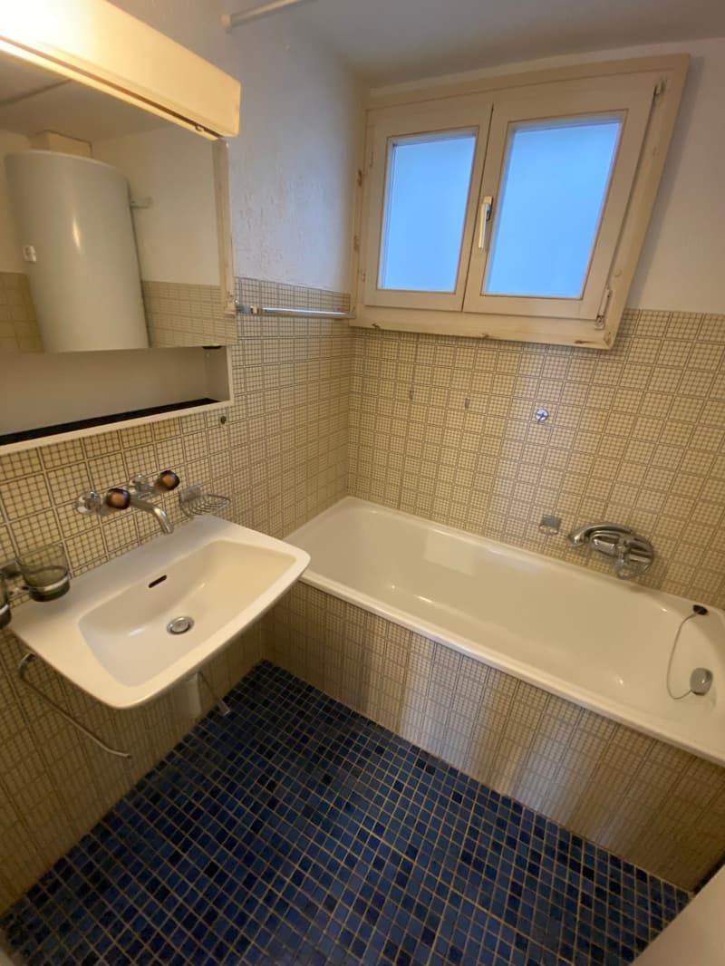 Bathroom with bathtub, sink, and mirror, blue tiles, white walls, and windows