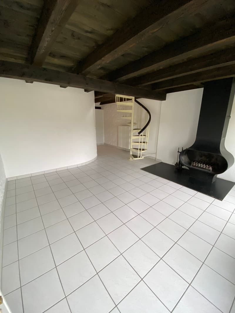 Empty room with white tiles, wooden ceiling, spiral staircase, fireplace