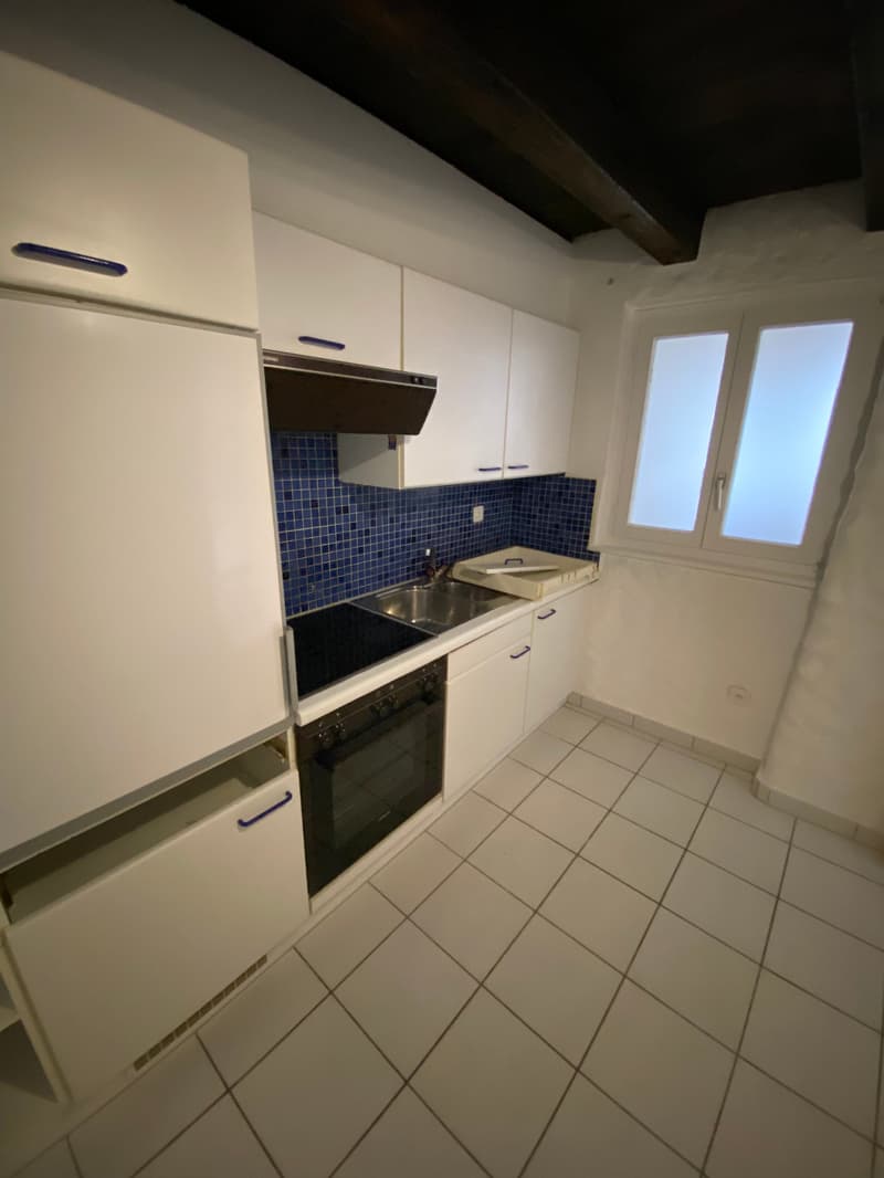 modern kitchen with white cabinets, blue tiles, black stove, sink, window