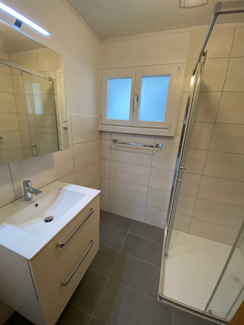 Bathroom with white tiles, white sink, mirror, shower, and window
