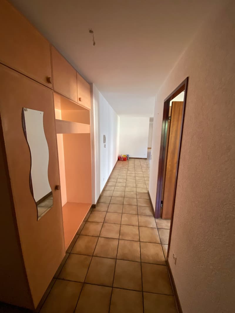 Empty hallway with tiled floor, wooden doors, and built-in cabinets with a mirror