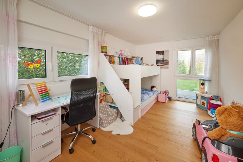 white bunk beds, study desk, black office chair, pink toy car, toys, white walls, wooden floor, round ceiling light