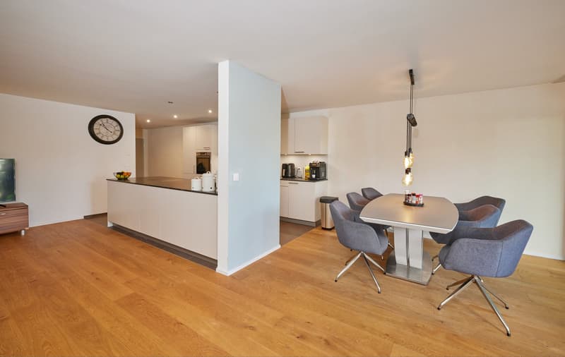 An open kitchen with modern cabinets, island, breakfast bar, appliances, and a dining area with round table and chairs.