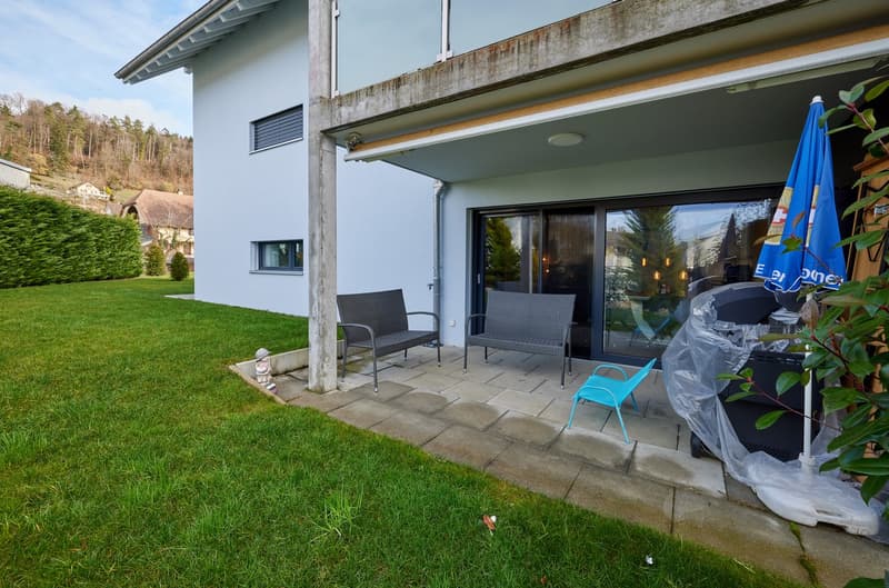 covered terrace with two chairs and blue plastic chair, closed sliding glass door, paved ground