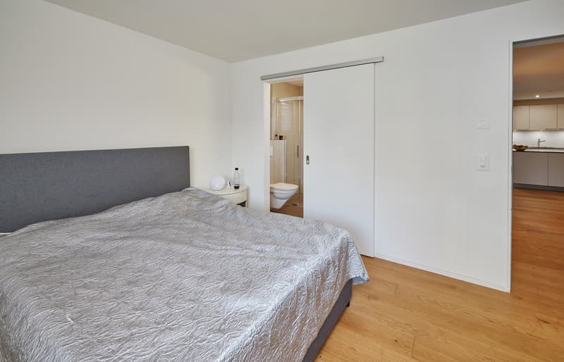 Bedroom with bed, nightstands, sliding door, wooden floors, clean and simple design.