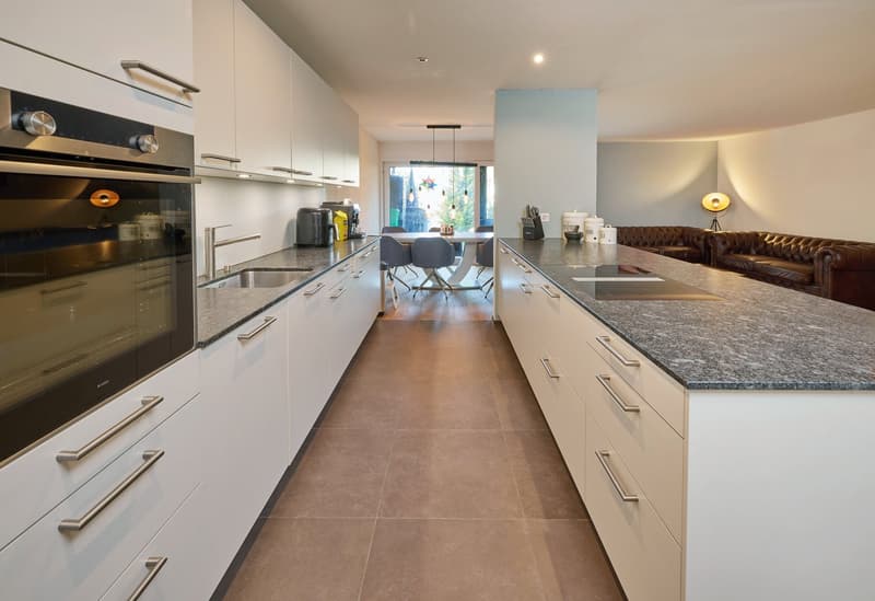 Modern kitchen with white cabinets, granite countertops, open view to dining area, large sink, gas stove, oven, and island
