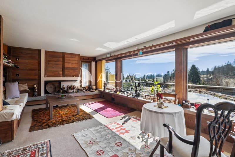 Das grosszügige Wohnzimmer mit Cheminée und Glasfront mit Blick aufs Biotop und die Berge.