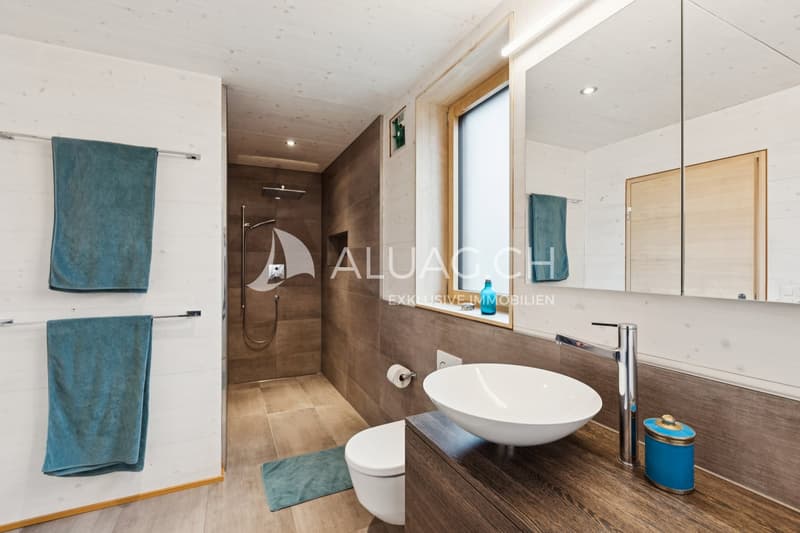 Blick im Familienbad Richtung der grossen begehbaren Dusche, rechts ein Fenster sowie eine Lüftungsventilator.