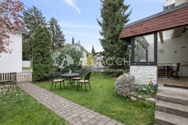 Die Hausumgebung mit Garten, Sträuchern und Bäumen sowie Platz zum Spielen. Rechts der Wintergarten.