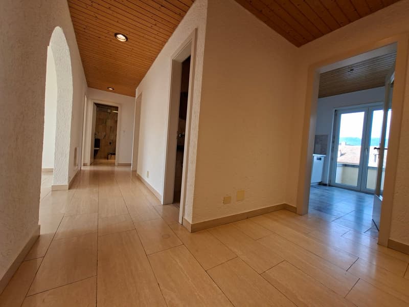 Empty hallway with wooden floors, white walls, wooden ceiling, and glass doors leading to a balcony with a view.