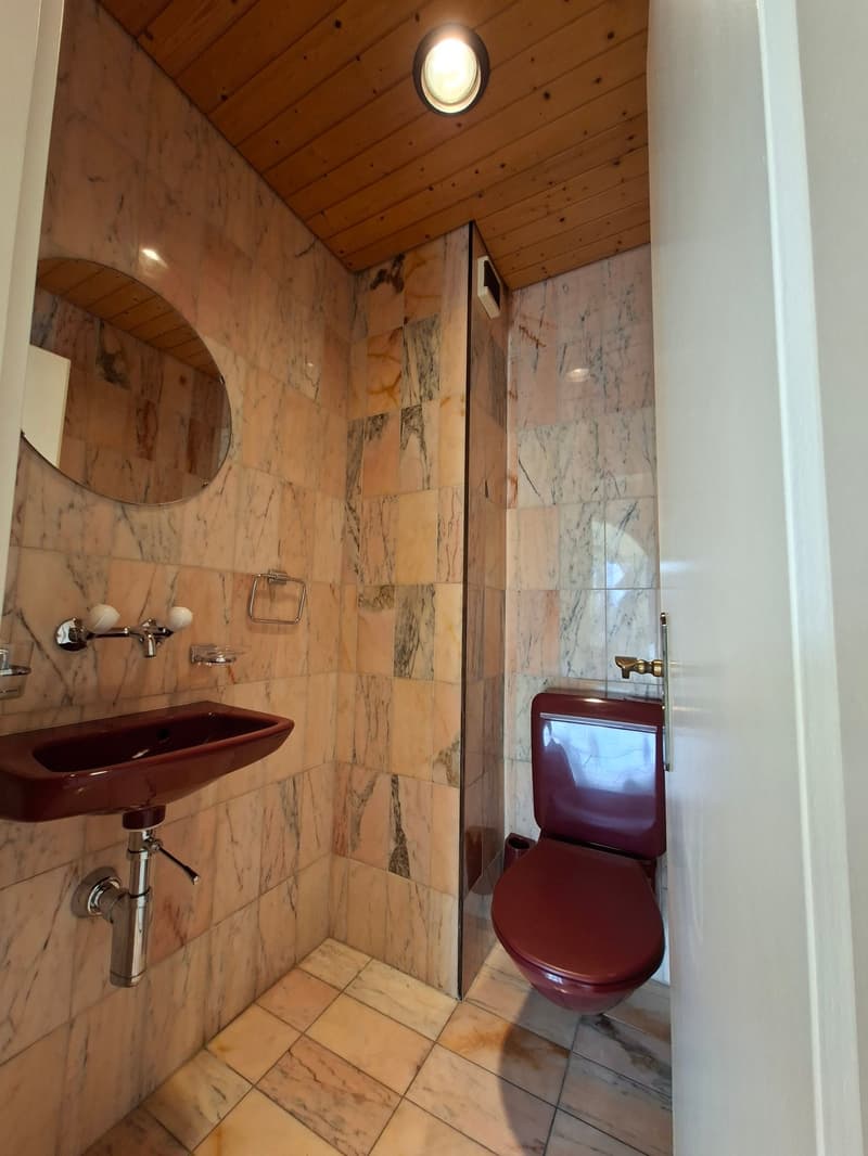 small bathroom with red toilet, sink, mirror, and tiled walls and floor