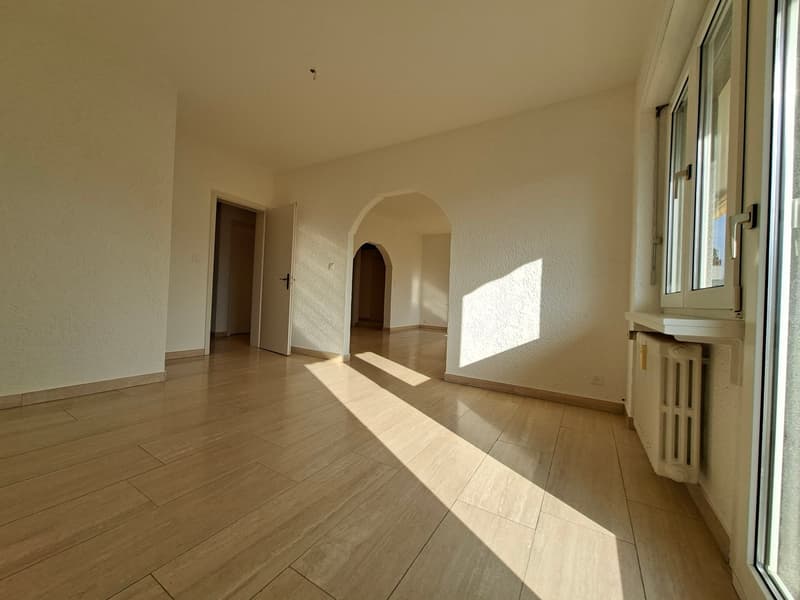 Empty room with wooden floors, white walls, two doors, and a window with a view outside.