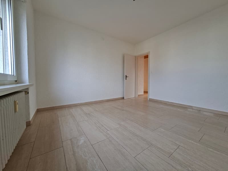 Empty room with white walls, wooden floor, window, and an open door leading to another room