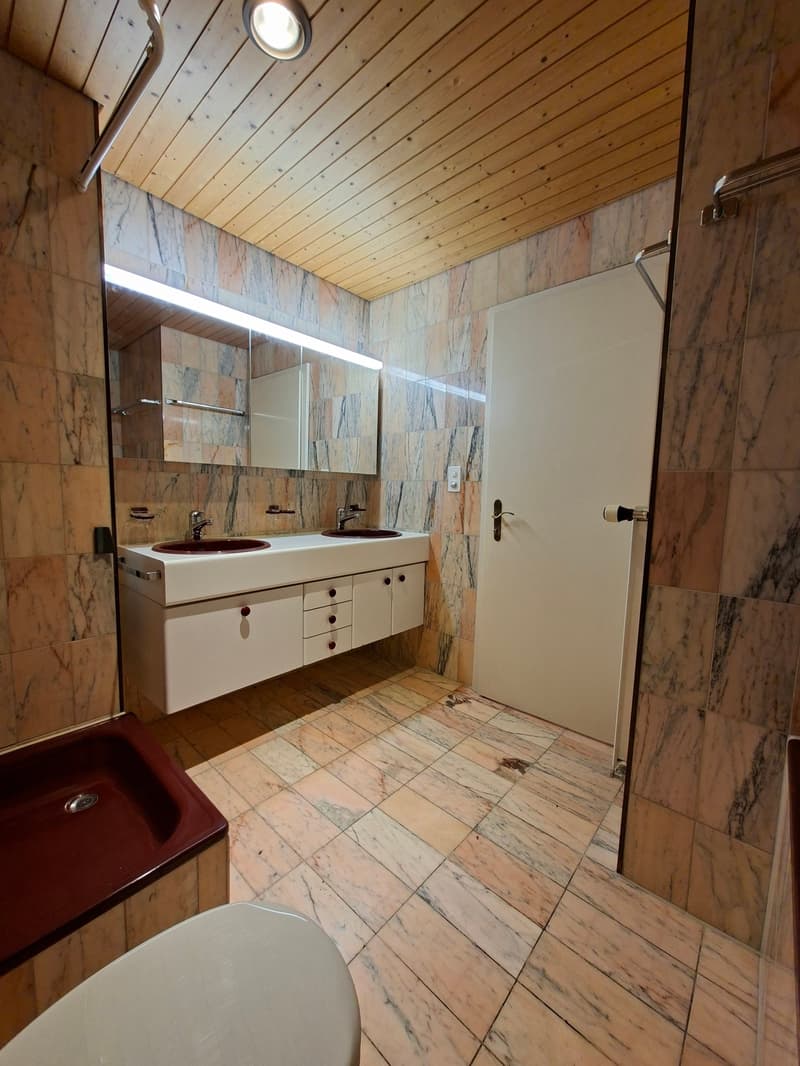 Double sink, bathtub, marble tiles, wooden ceiling, white door, mirrors