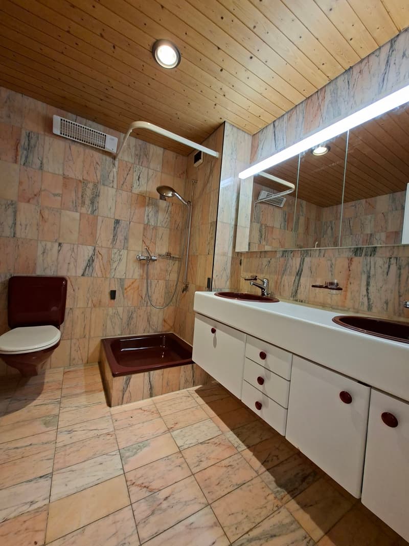 Bathroom with marble tiles, wooden ceiling, two sinks, bathtub, toilet, shower, mirror, and air conditioning unit.