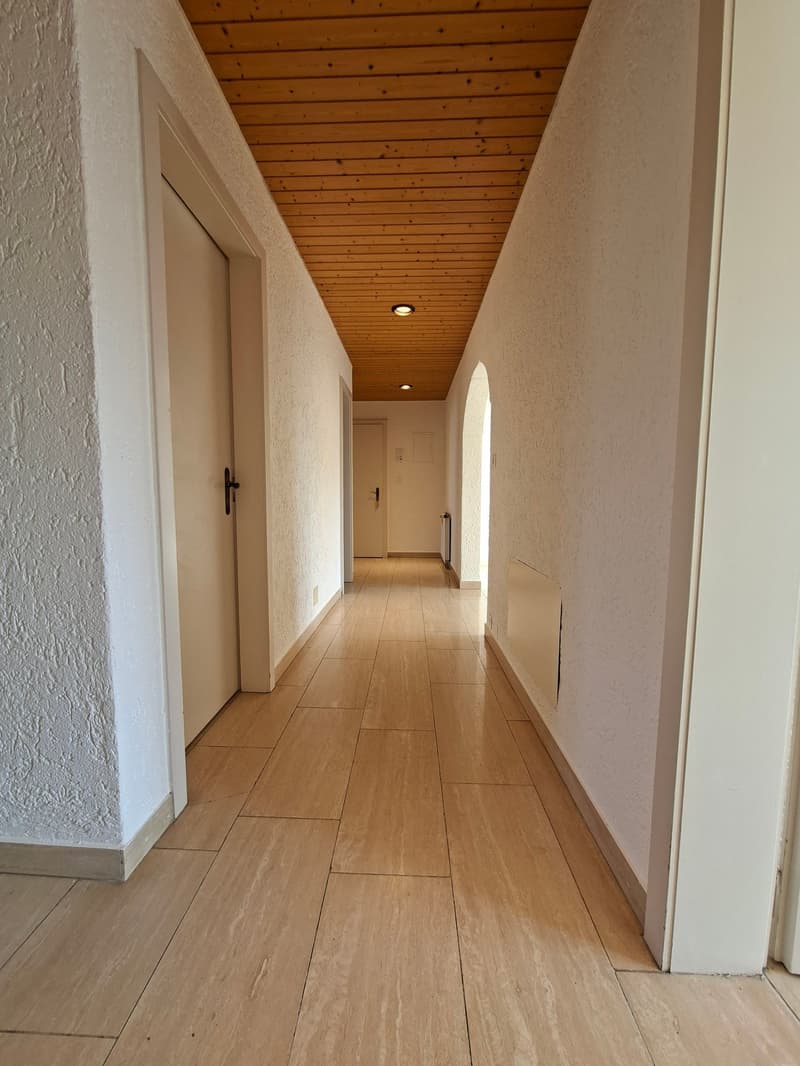 Empty hallway with wooden floor, white walls, wooden ceiling, two doors, and a radiator.