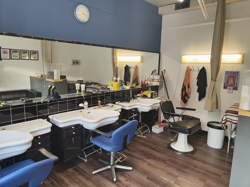 a hair salon with shampoo bowls, barber chairs, a barber's chair, and a large mirror