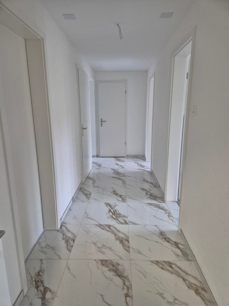 Marble flooring, white walls, doors on either side, clean and empty.