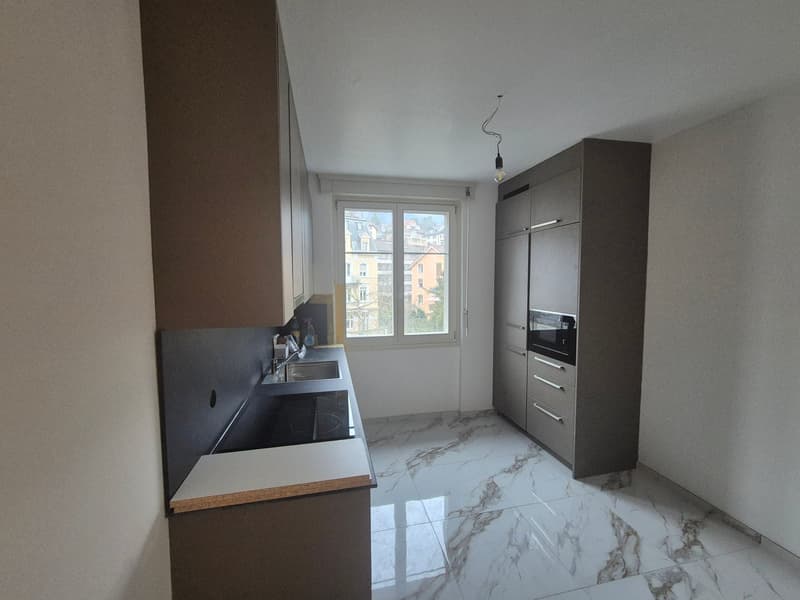 Modern kitchen with marble countertops, stainless steel appliances, white cabinetry, double sink, induction cooktop, built-in oven, kitchen faucet.