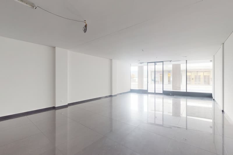 Large open space with white walls, high ceilings, and large windows providing ample natural light. The floor is covered with shiny, reflective tiles. The space appears to be a commercial or office area, ready for customization and furnishing.