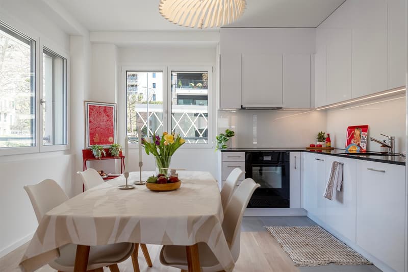 Dining room with a table, chairs, and a kitchen area with a black oven and white cabinets