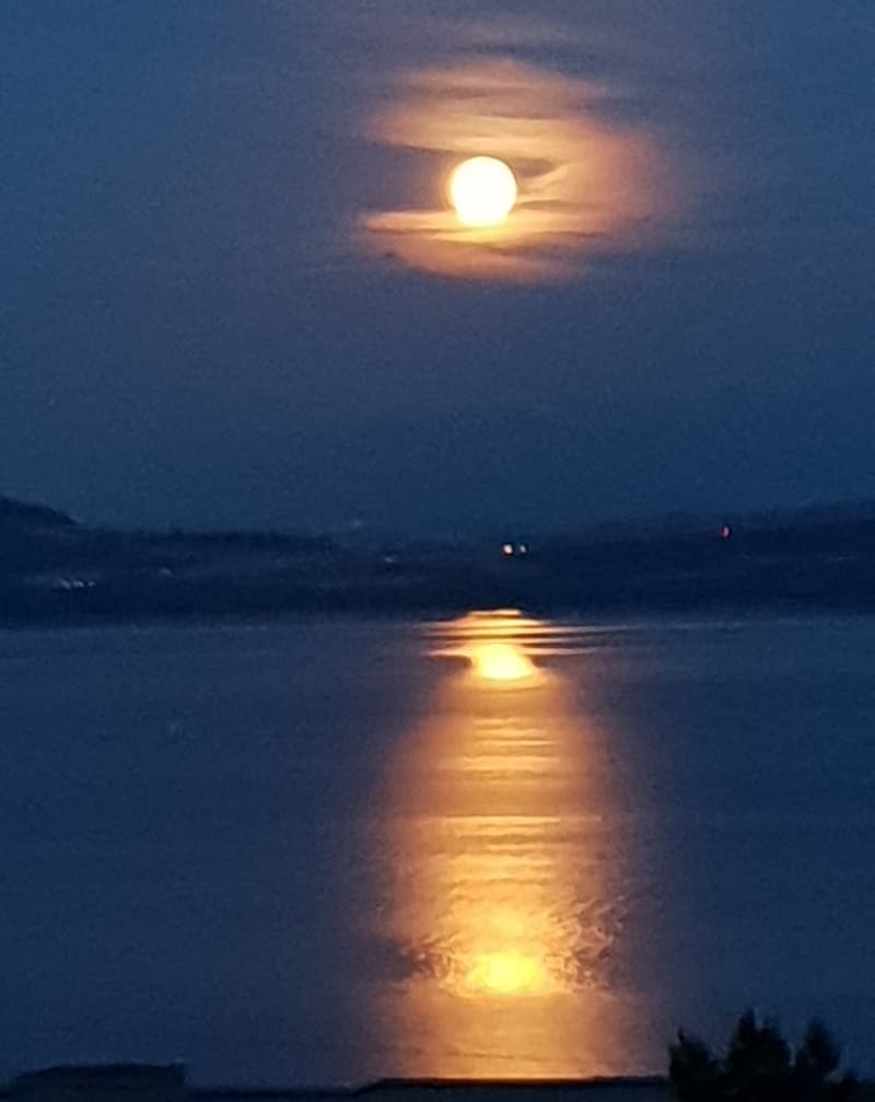 full moon rising over a lake with mountains in the background