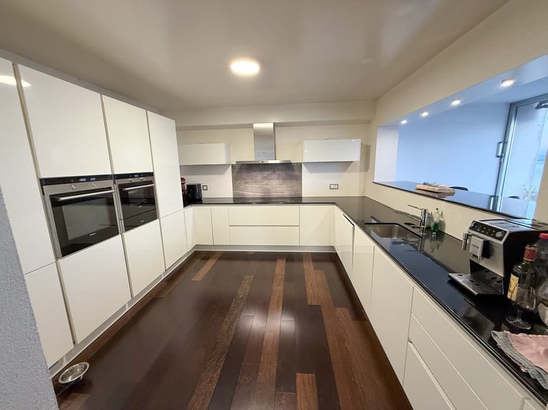 Modern kitchen with white cabinets, black granite countertops, integrated dishwasher, washing machine, two ovens, island with seating, and large window.